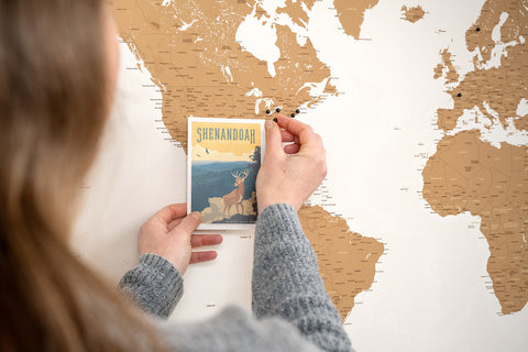 Frau pinnt eine Postkarte aus den USA an eine Weltkarte als Leinwand